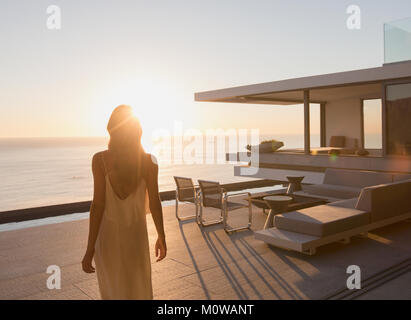 Woman walking on tranquil sunset modern, luxury home showcase exterior patio with ocean view Stock Photo