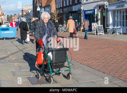 Elderly woman with wheeled rollator (wheeled zimmer frame walking aid) in a pedestrianise shopping area in Chichester, West Sussex, England, UK. Stock Photo