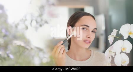 Brunette woman applying makeup with powder brush Stock Photo