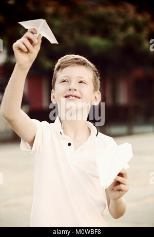 happy boy playing with simple paper airplane toy on sunny day in town ...