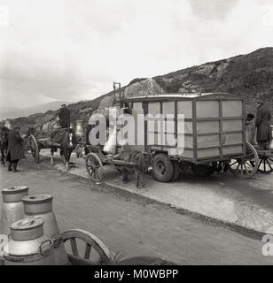 1950s, an historical picture showing local farmers and small-holders with their horse and carts filling their milk churns with milk from a mobile dispensing truck parked on a concrete platform beside a country road in rural Ireland. Stock Photo