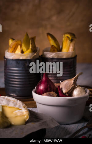 Vertical photo of white bowl full of color onions and garlic cloves. The bowl is placed on blue wooden vintage board with fried potato strips in old c Stock Photo