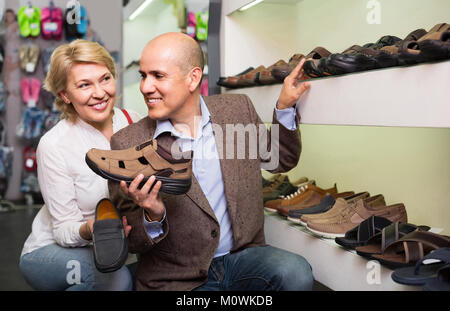 Two smiling retirees together choosing pair of shoes for men in shoe store Stock Photo