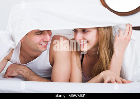 Young adults lying in family bed under sheet Stock Photo