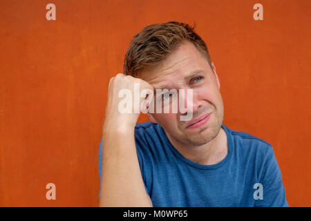 Close up portrait of caucasian disappointed stressed young man on red background. He is about to cry. Negative human emotions Stock Photo