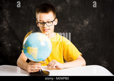 Kid looking at small globe on the desk Stock Photo