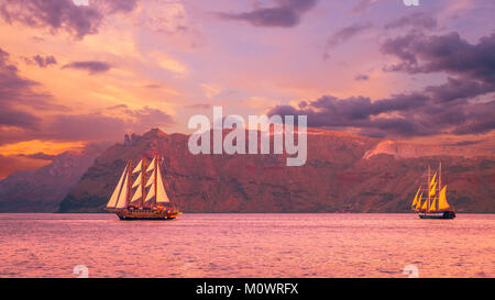 Sailboat in Santorini, Greece. Sailing ship navigate near an island in Cyclades. The photo is taken at sunset. Stock Photo