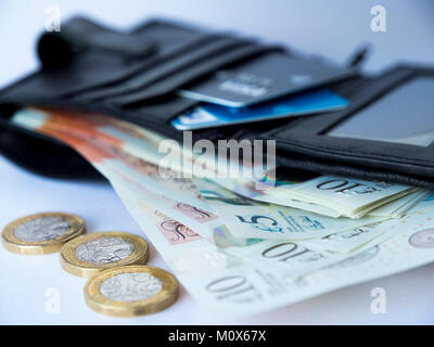 A black wallet containing credit or debit cards and five and ten pound notes fanned out with three pound coins at the front Stock Photo