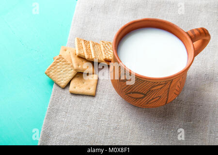 clay cup with milk stands on a turquoise background on linen napkin. near the a cup are scattered crackers. Stock Photo