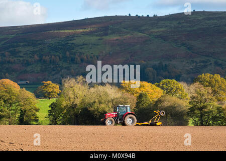 A farm tractor working in a field beneath the Long Mynd at Myndtown in the Shropshire Hills, England, UK Stock Photo