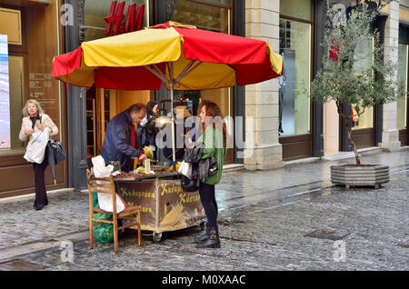 Food vendor with colourful umbrella over his portable cart with charcoal grill selling roasted corn on the cob, Emou street, Athens Stock Photo