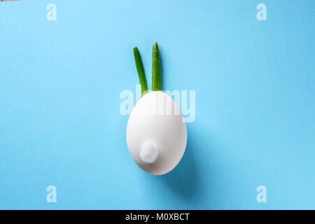 Egg shell and feathers green onion imitation rabbit bunny on blue colored paper background. Food concept minimal Easter Stock Photo