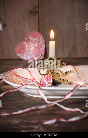Little golden Cupid, with candle and paper hearts. Stock Photo