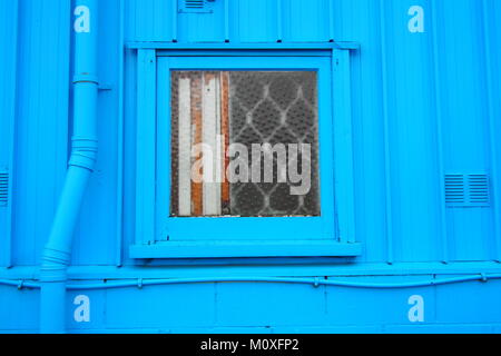 small window on blue corrugated metal wall Stock Photo