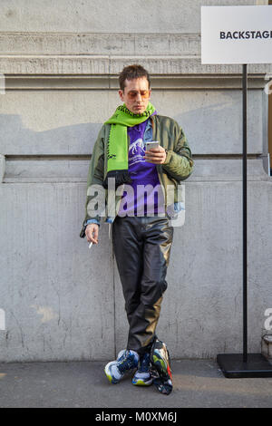 MILAN - JANUARY 13: Man with olive green bomber jacket and purple sweater looking at smartphone before Marni fashion show, Milan Fashion Week street s Stock Photo