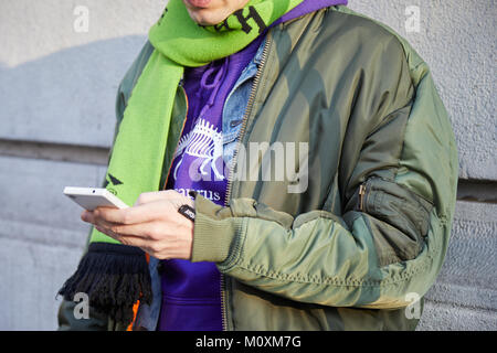 MILAN - JANUARY 13: Man with green bomber jacket, scarf and purple sweater looking at phone before Marni fashion show, Milan Fashion Week street style Stock Photo