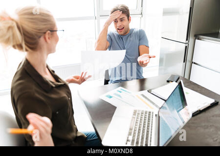 Young busy angry man has a quarrel with his woman while working with papers at home Stock Photo