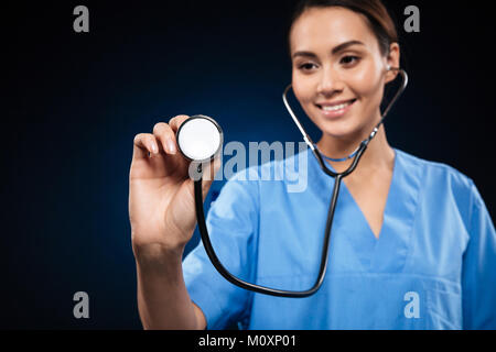 Portrait of smiling brunette caucasian doctor in blue uniform using stethoscope isolated over black Stock Photo
