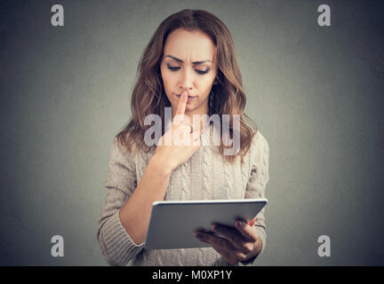 Young casual woman watching tablet and looking puzzled touching lips. Stock Photo