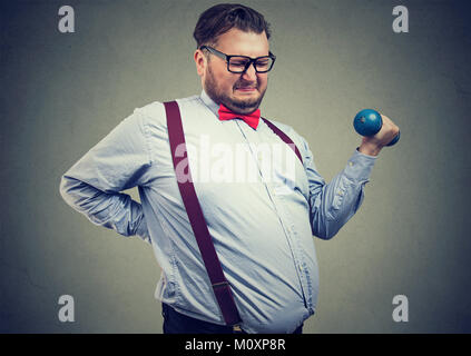 Young overweight man applying force to lift dumbbell frowning. Stock Photo