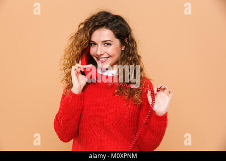 Portrait of a smiling satisfied girl talking on a landline telephone isolated over beige background Stock Photo
