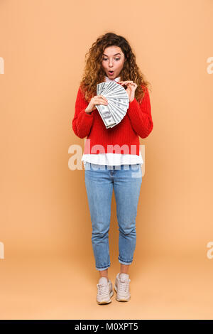 Full length portrait of a satisfied cheery girl counting money banknotes and celebrating isolated over beige background Stock Photo