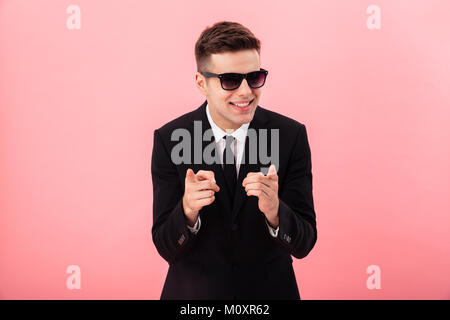 Happy cheerful businessman in official suit smiling to aside and smiling isolated over pink Stock Photo