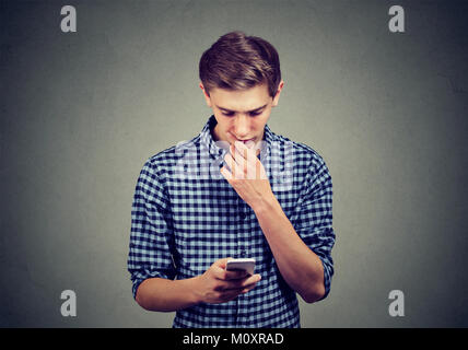 Casual teenager watching smartphone looking confused with complicated gadget. Stock Photo
