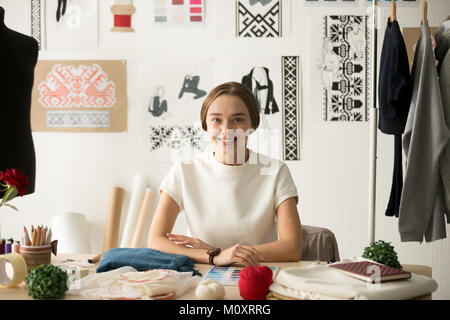 Smiling attractive fashion designer sitting at workplace looking Stock Photo