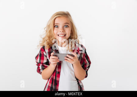 Portrait of an excited little girl holding mobile phone and looking at camera isolated over white background Stock Photo