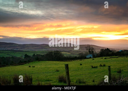 over looking an Irish field with mountains in the distance and a golden sunset reflecting off of the clouds. Stock Photo