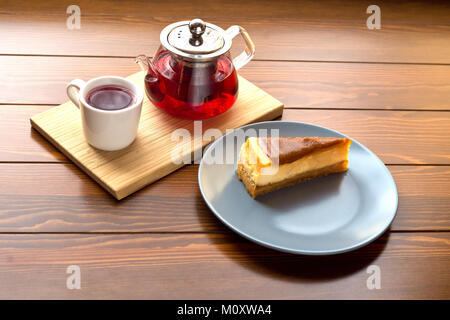 Transparent teapot with hot tea on the stand along with chocolate cheesecake