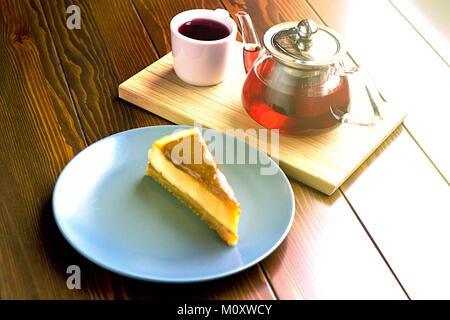 Transparent teapot with hot tea on the stand along with chocolate cheesecake