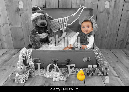 3 month old mixed race baby boy playing in toy box vintage suitcase full of  toys Stock Photo
