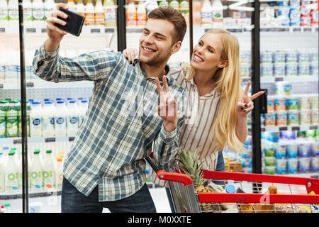 Happy young couple taking a selfie with a smartphone while shopping at the supermarket Stock Photo
