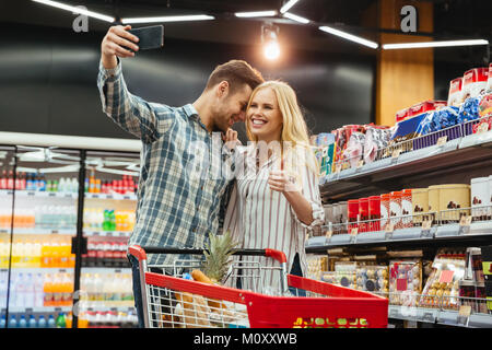 Happy couple showing thumbs up while taking a selfie at supermarket Stock Photo