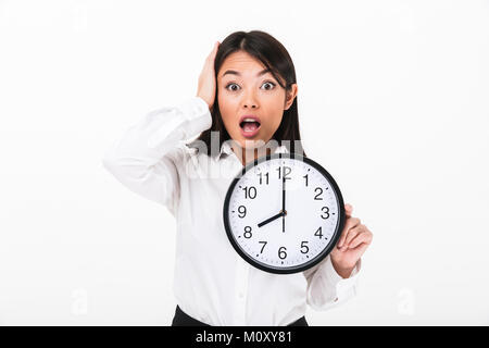 Portrait of a terrified asian businesswoman holding wall clock and looking at camera isolated over white background Stock Photo