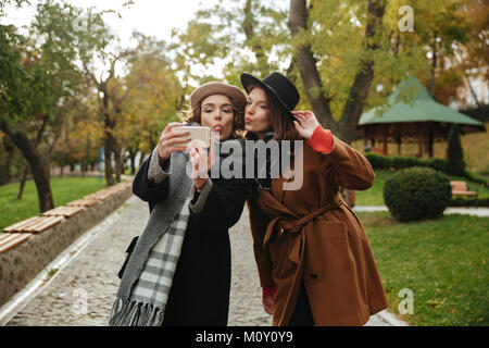 Portrait of two pretty girls dressed in autumn clothes taking a selfie while standing outdoors Stock Photo