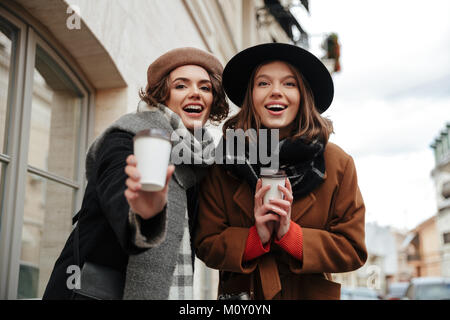 Portrait of two pretty girls dressed in autumn clothes walking on a city street with coffee cups Stock Photo