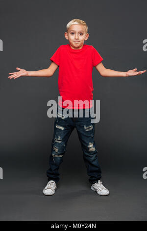 Image of confused little boy child standing isolated over grey background. Looking camera. Stock Photo