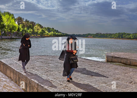 Isfahan, Iran - April 24, 2017: Three unknown women in a black religious veil stroll by the river Zayandeh. Stock Photo