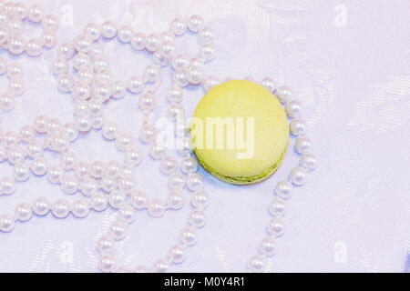 Top view of a macarons dessert with pearl necklaces lie on a table on a white tablecloth. Close-up Stock Photo