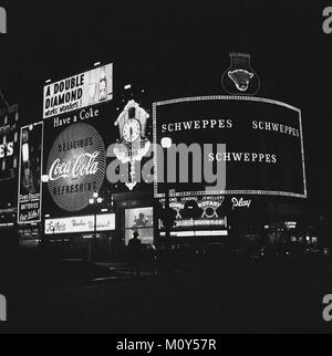 1960s, historical picture showing the famous neon advertising signs and slogans lighting up the night at the Piccadilly Circus roundabout in London's west end, England, UK. Stock Photo