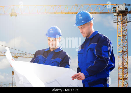 Two Young Male Architect Looking Into Blueprints At Construction Site Stock Photo