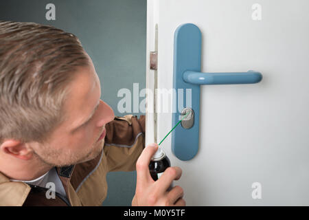 Close-up Of Repair Man Spraying Oil In Keyhole Of White Door Stock Photo