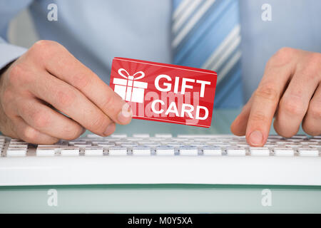 Businessman's Hand Holding Red Gift Card On Keyboard Over The Desk Stock Photo