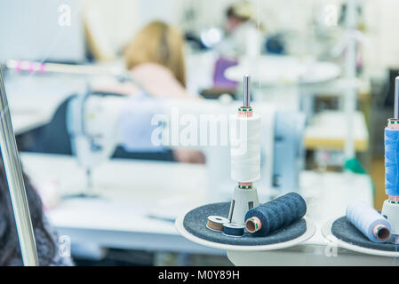 Spools of thread in the sewing equipment with blurred working tailors on background. The concept of sewing production. Selective focus, space for text. Stock Photo