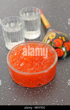 Red caviar in a glass bowl. Wooden spoon painted in traditional style Khokhloma and shot glass of vodka. Stock Photo
