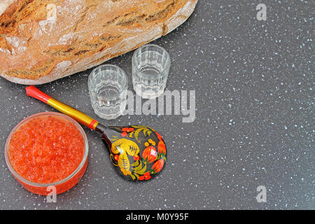 Red caviar in a bowl and fresh baked bread. Wooden spoon painted in traditional style Khokhloma and shot glass of vodka. Traditional russian food. Stock Photo