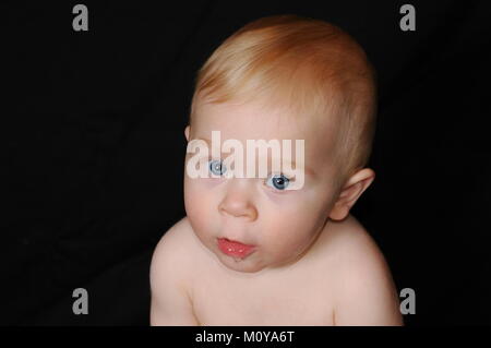 Nine month old baby boy low-key portrait with black back drop.  Looking directly at camera. Soft lighting. Head-shot with baby only in the frame. Stock Photo